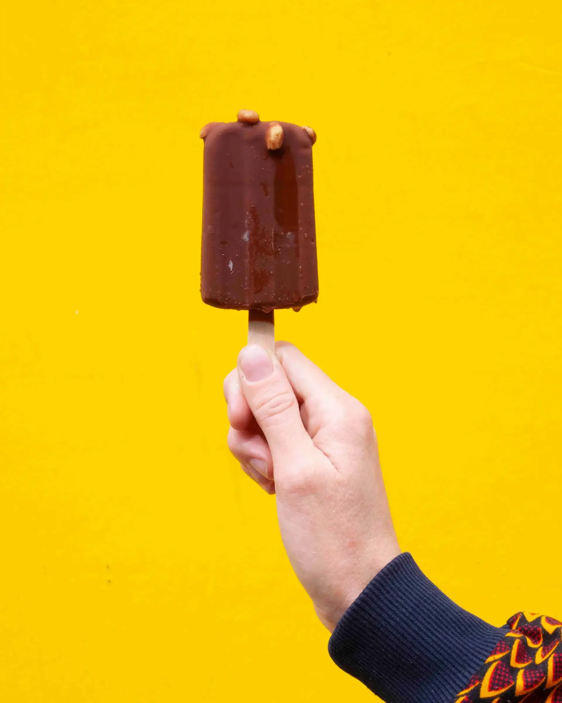 Une main qui tient une glace au chocolat devant un fond jaune